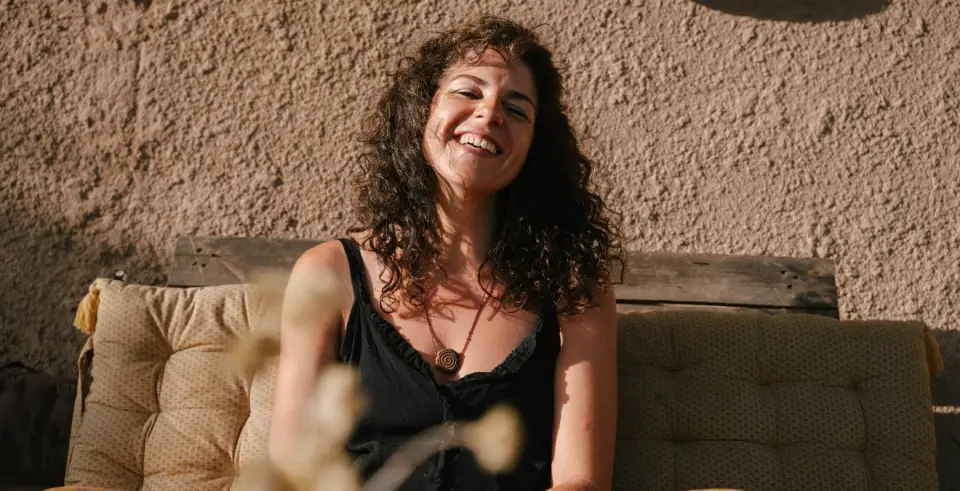 Cristina Duran somrient, asseguda al sol en un banc amb coixins